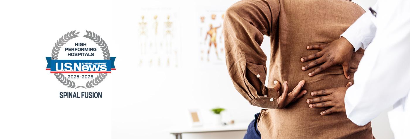 Close up photo of a doctor examining a patient's back. The image includes a badge that reads "US News & World Report High-performing Hospitals, Spinal Fusion, 2025-2026."