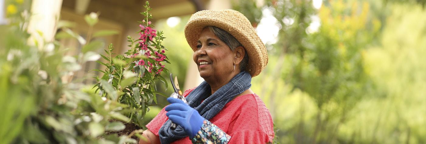 An older woman works in her garden while wearing a straw hat and gardening gloves