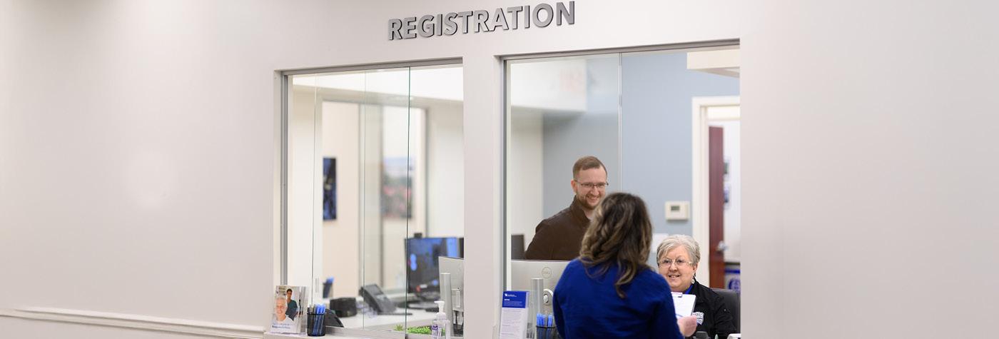 A patient checks in at a registration window. 