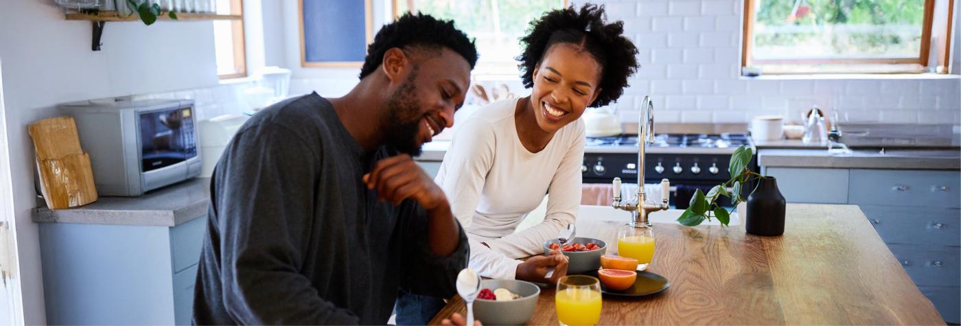 A man and woman sit together at a table smiling while eating breakfast foods. 