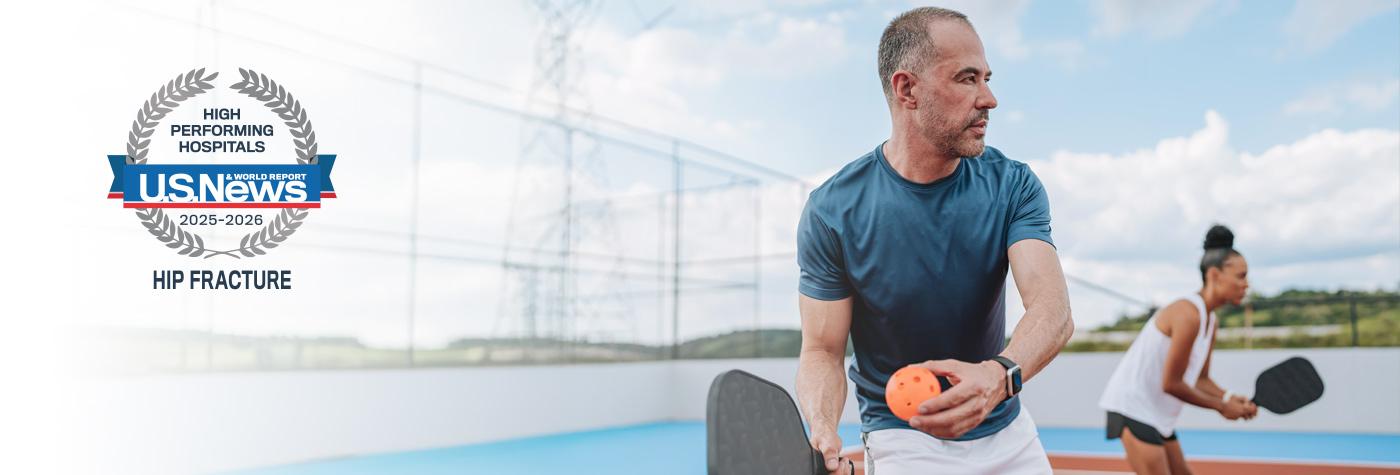 A man and woman play pickleball. A badge superimposed over the photo reads "US News & World Report High-performing Hospitals, 2025-26, Hip Fracture."