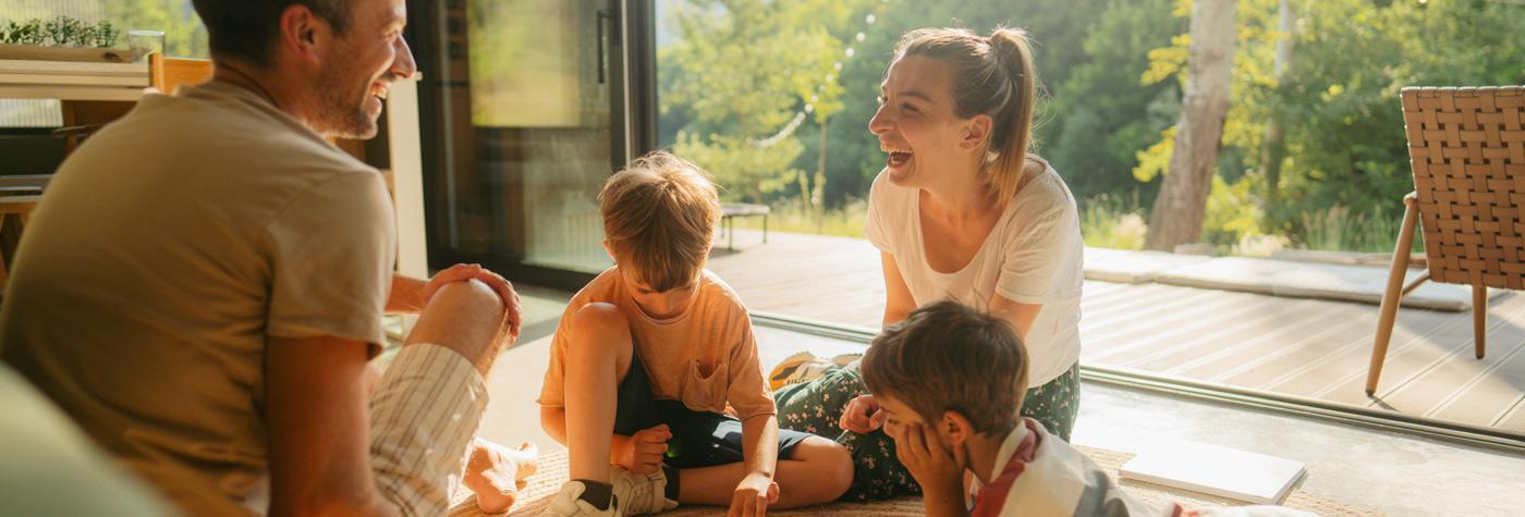 A man, a woman and two young children sit together on a floor, playing and laughing. 