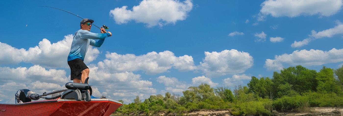 A man stands on a fishing boat while casting a line.