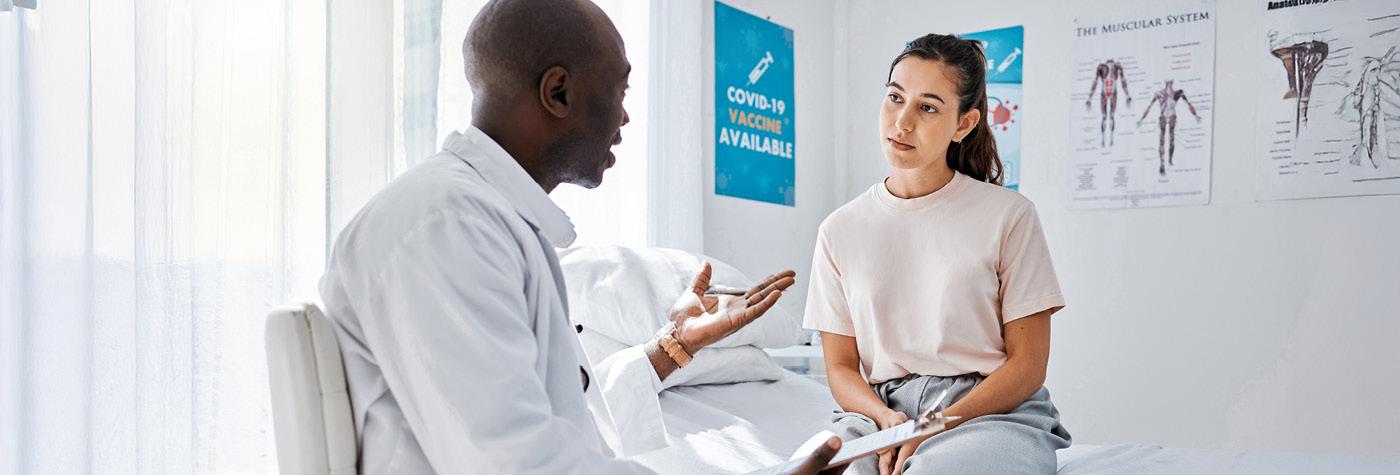 A woman sits on an exam table and talks to her doctor.