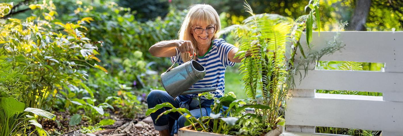 A smiling woman waters plants in her garden.