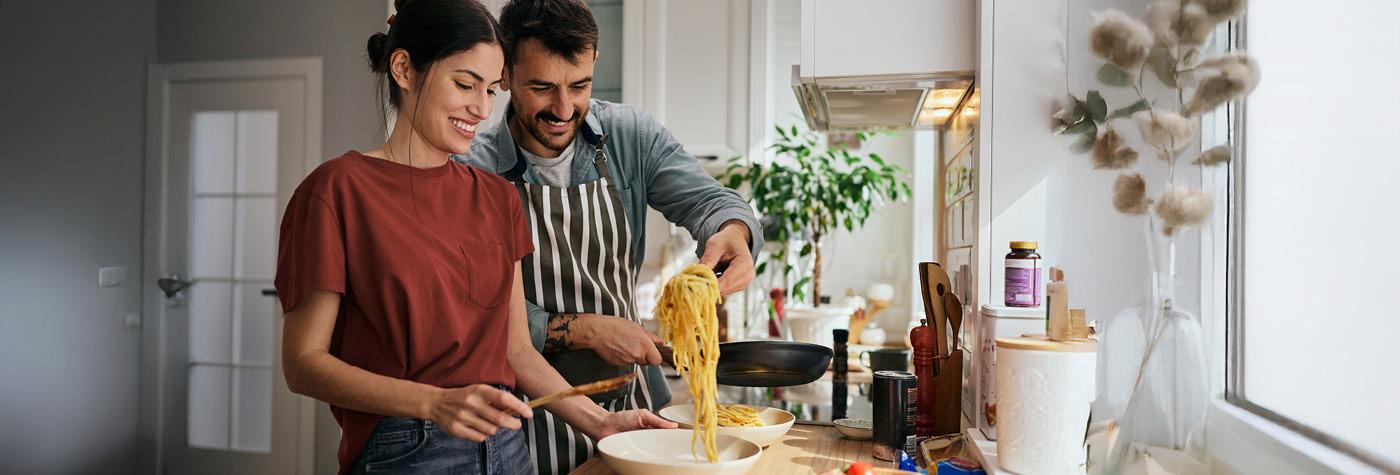 A man and woman prepare pasta together in a kitchen
