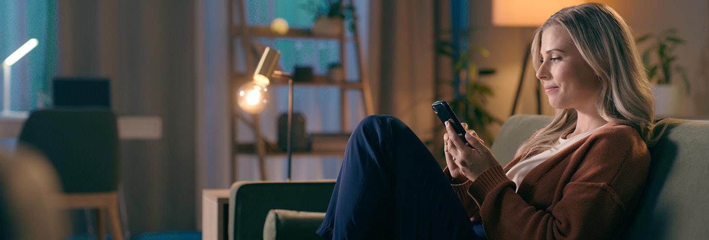 A woman sits on her sofa while looking at her smart phone.