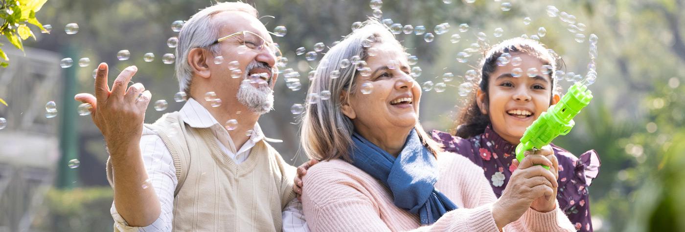 Two adults and a child sit outdoors, interacting with bubbles in a park setting.