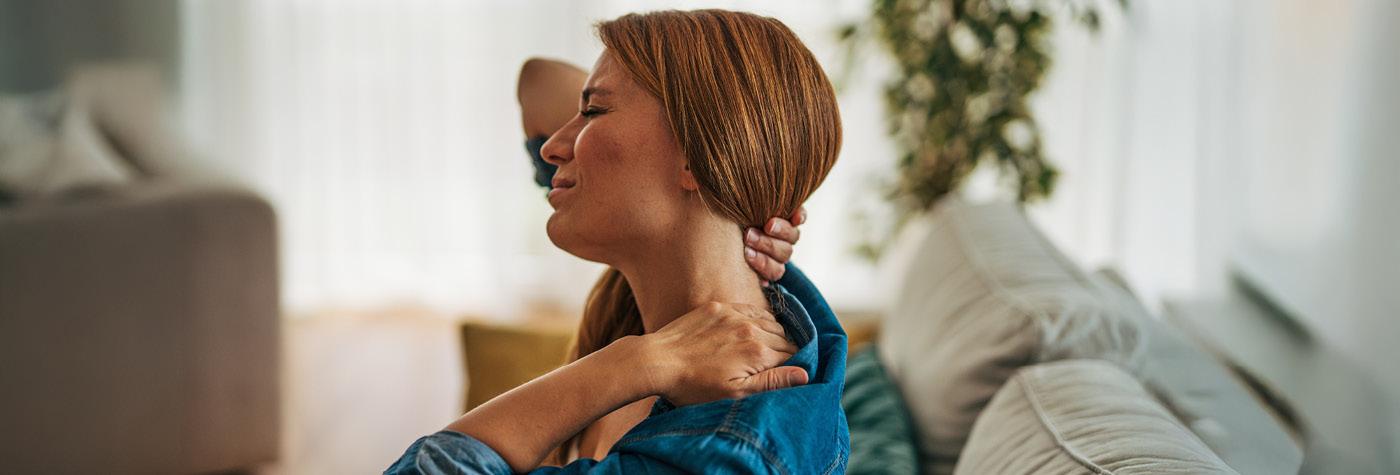 A woman wearing a blue blouse holds the back of her neck, showing that she's in pain. 