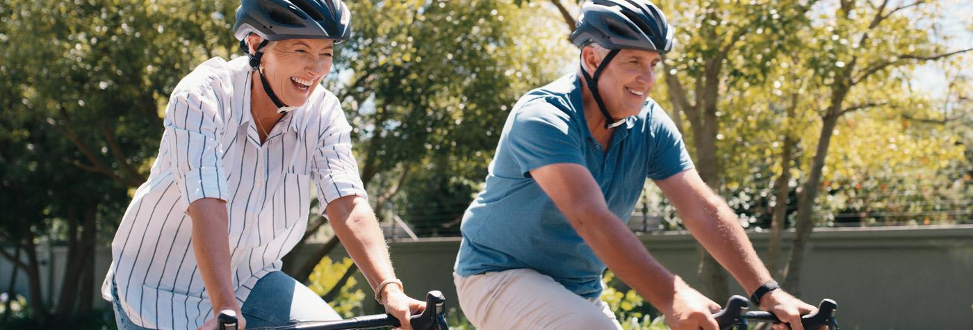 A man and woman smile while biking side by side. Both are wearing helmets.