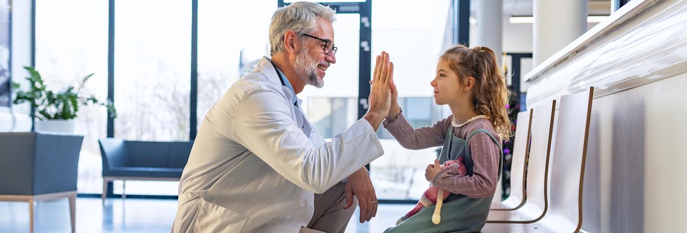 A doctor gives a high five to a young girl who is holding a stuffed animal.