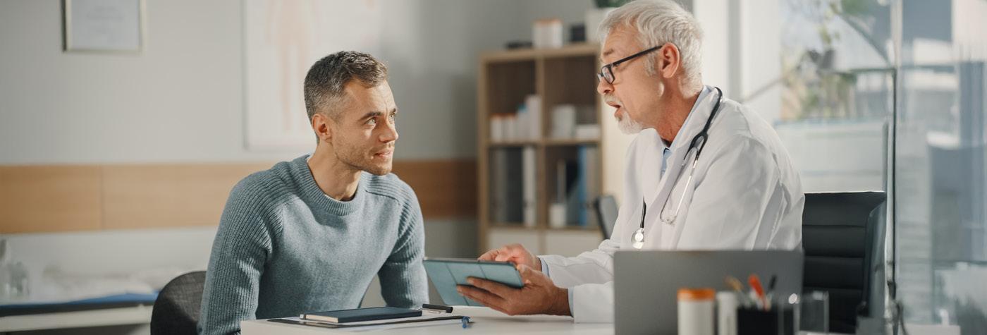 A man and his doctor sit at a desk at have a conversation.
