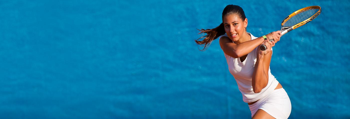 A woman standing in front of a blue background swings a tennis racket.