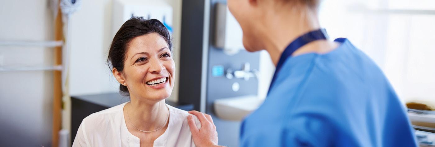 A woman smiles while speaking to a doctor wearing blue scrubs