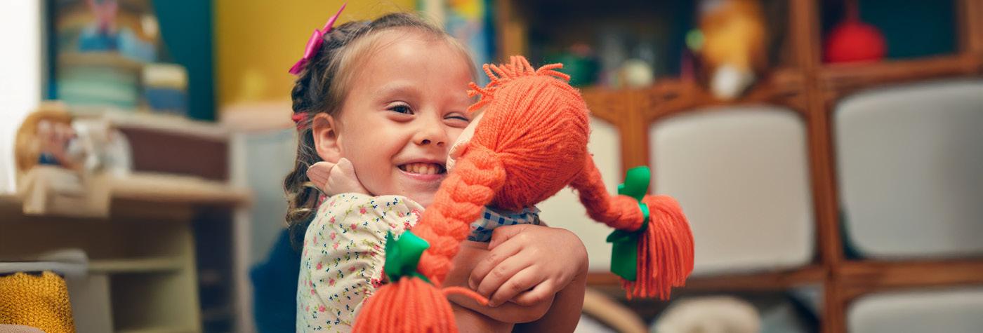 A young girl embraces a doll with orange yarn hair.
