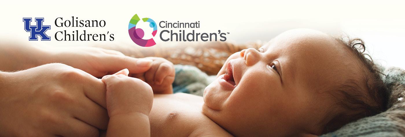 An adult holds a baby's hands while the baby looks toward them smiling. Superimposed on the photo are the Golisano Children's at UK and Cincinnati Children's logos.