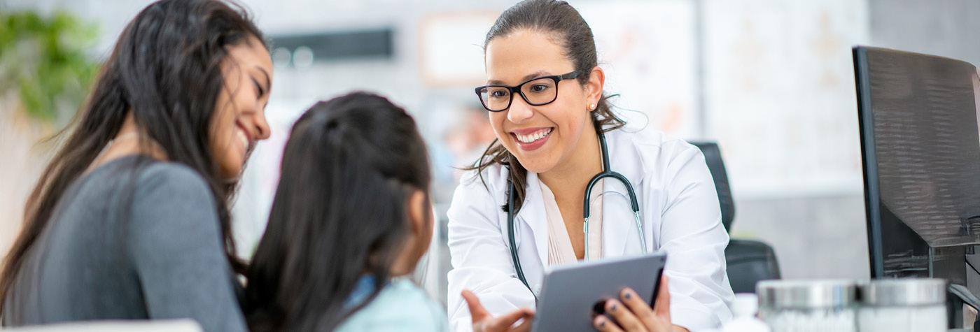 A doctor points to information on a tablet while speaking to a girl and her mother.