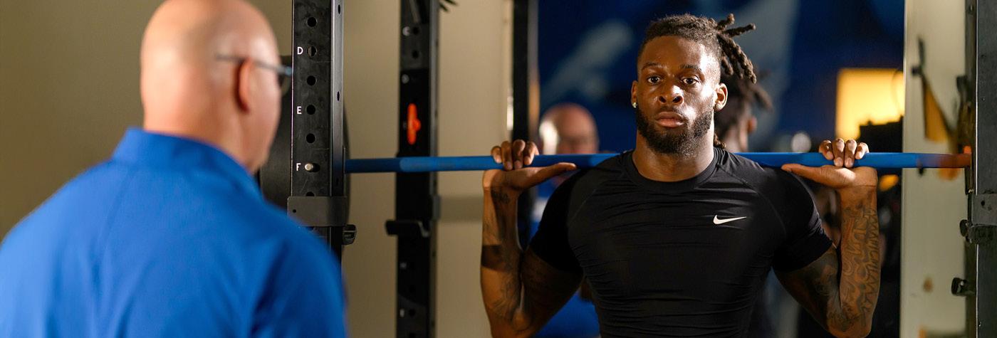 Physical therapists observes athlete using squat rack