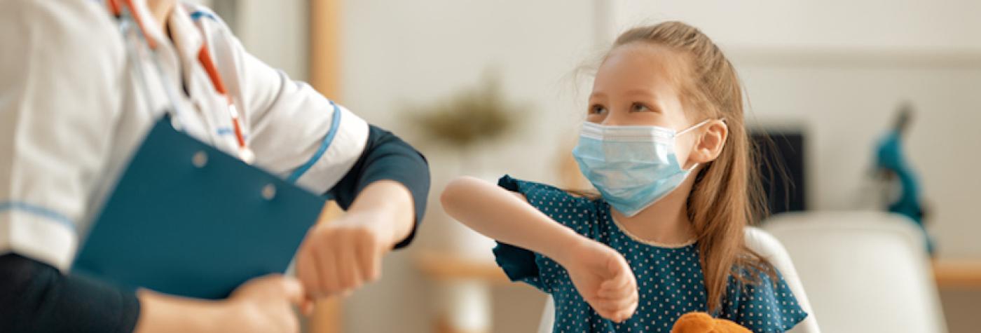 Young girl wearing surgical mask bumps elbows with nurse