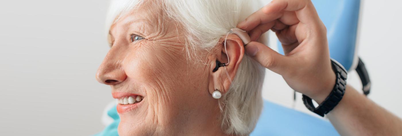 An audiologist places a hearing aid in a patient's ear.
