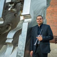 Adiel Nájera poses with his trumpet in front of an outdoor sculpture on the University of Kentucky campus.
