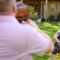 Sarah Beth throws a ball to her father, who is standing in front of the camera. She is wearing a grey shirt, black shorts with pink polka dots, and a colorful softball glove.