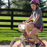 With a pink helmet on her head, Sarah Beth rides her white and pink bicycle outside.
