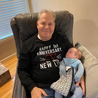 James Fielding holds a baby while wearing a t-shirt that reads, &quot;Happy 1st Anniversary to My New Liver.&quot;