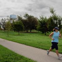 wide angle view of Jeanne Hartman, further to right of image, running at a park with a water tower that says UK in the background