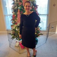 Jeanne Hartman smiling in front of a Christmas tree. She's wearing a long black dress.