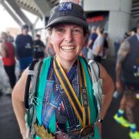 Jeanne Hartman smiles at a camera following a race, and wearing several medals.