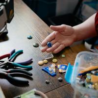 Nicola Allen holds sewing buttons with others strewn on the table before here. Only Nicola's hand is visible.