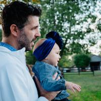 Dr. Kyle Riggs looks off camera with a child in his hands. They're on a farm.
