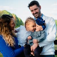 Closer portrait of the riggs family. Marya is holding one toddler, who's kissing st the other. Kyle Riggs holds that one.