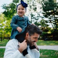 One of Dr. Kyle Riggs' children rides on his shoulders. The child looks toward the camera.