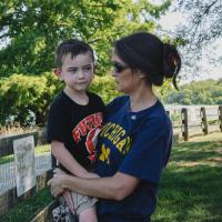 Granger Smith is held by his mother while the two stand near a fence at a park. Granger has a mischievous look on his face.