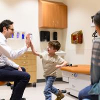 Granger Smith, center, gives a high five to Dr. David Neil Toupin, left, who's seated in a rolling chair. Granger's mother is slightly visible to the right.