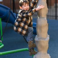 Granger Smith, smiling toward the camera, climbs a small playground fixture shaped kind of like a rock