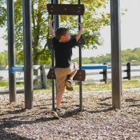 A medium-wide shot of Granger Smith climbing up a playground ladder. He's looking excitedly offscreen toward something or someone