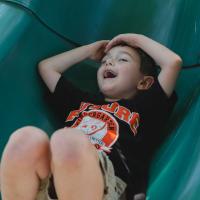 Granger Smith slides down the end of a playground slide, excited with his hands over his head.