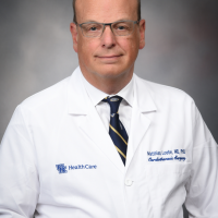 Dr. Matthias Loebe poses against a gray background wearing a white medical coat with her name written on it.