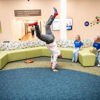 Dr. Scottie Day standing on his hands in a lobby area as two kids watch in delight