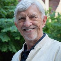 Chuck Gutenson smiles toward camera, posed in a white blazer against some foliage