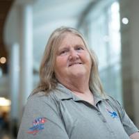 Linda Baxter poses for a portrait against the windows of the lobby in UK Albert B. Chandler Hospital. She's wearing a gray polo.