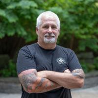 Tom Coleman poses for a portait, wearing black t-shirt in a patio area