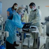 A group of medical professionals prepare for a procedure on a table. A clock reads 9:47 above them