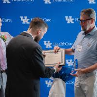 Michael Hudkins holds a certificate and is mingling with men in suits