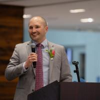 Zach Warriner speaks from a podium, smiling