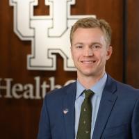 Dr. Kluemper, an adult white man with blonde hair, smiles in front of a UK HealthCare logo. He is wearing a navy suit and a green tie.