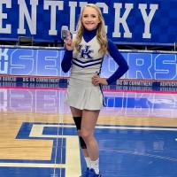 Allie poses on a UK basketball court in her cheerleading uniform and knee brace.